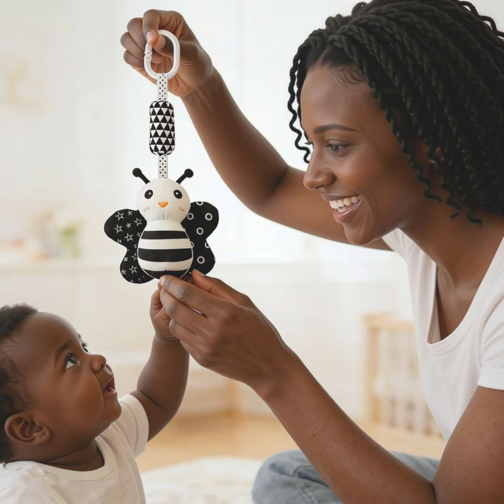 Mother holding up a high-contrast ladybug visual toy during tummy time encouraging newborn baby to reach and build motor skills, available from Senso-Blanky