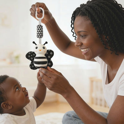 Mother holding up a high-contrast ladybug visual toy during tummy time encouraging newborn baby to reach and build motor skills, available from Senso-Blanky