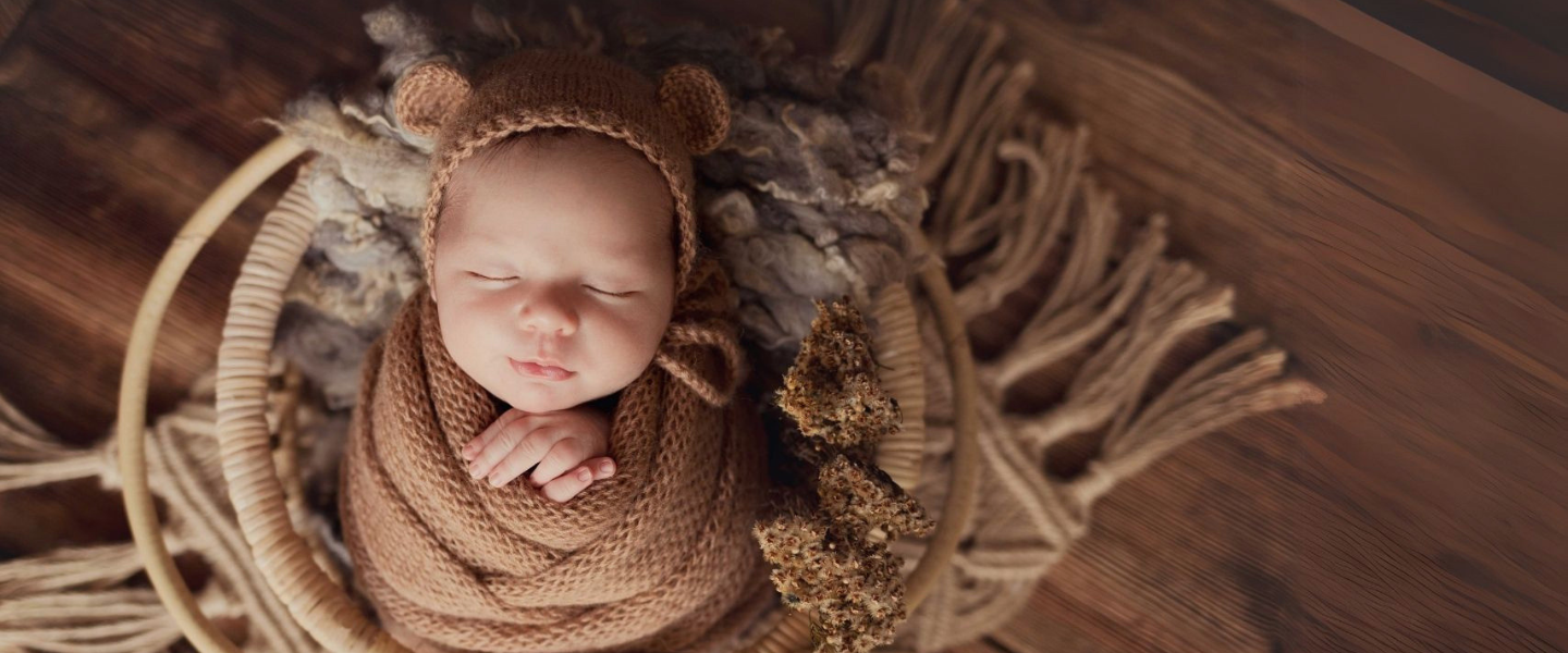 Senso-Blanky Hero Baby wrapped in brown knitted swaddle and wearing a bear hat in a wooden basket.