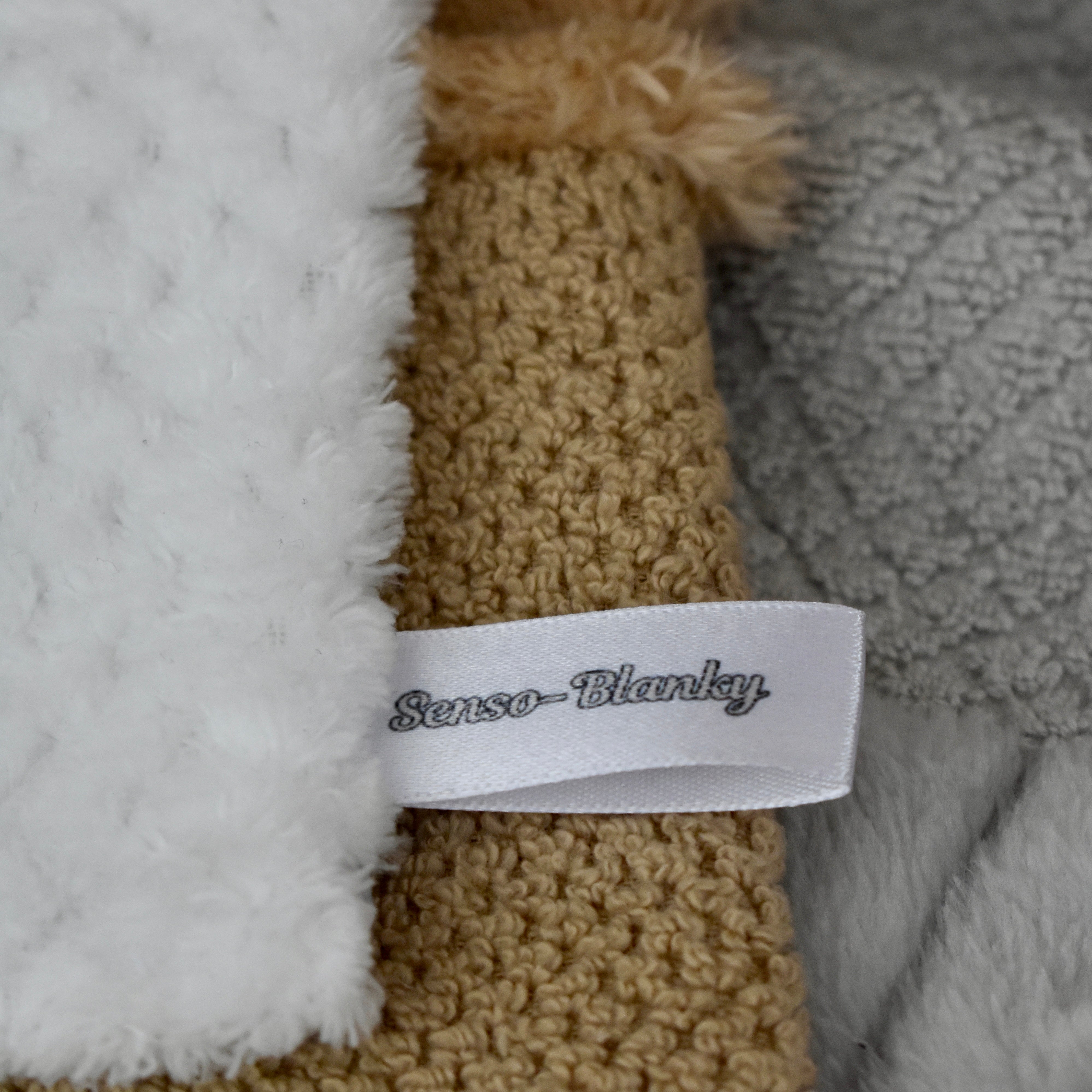 Close-up of a blanket with 'Senso-Blanky' label, featuring textured fabric and a brand name.